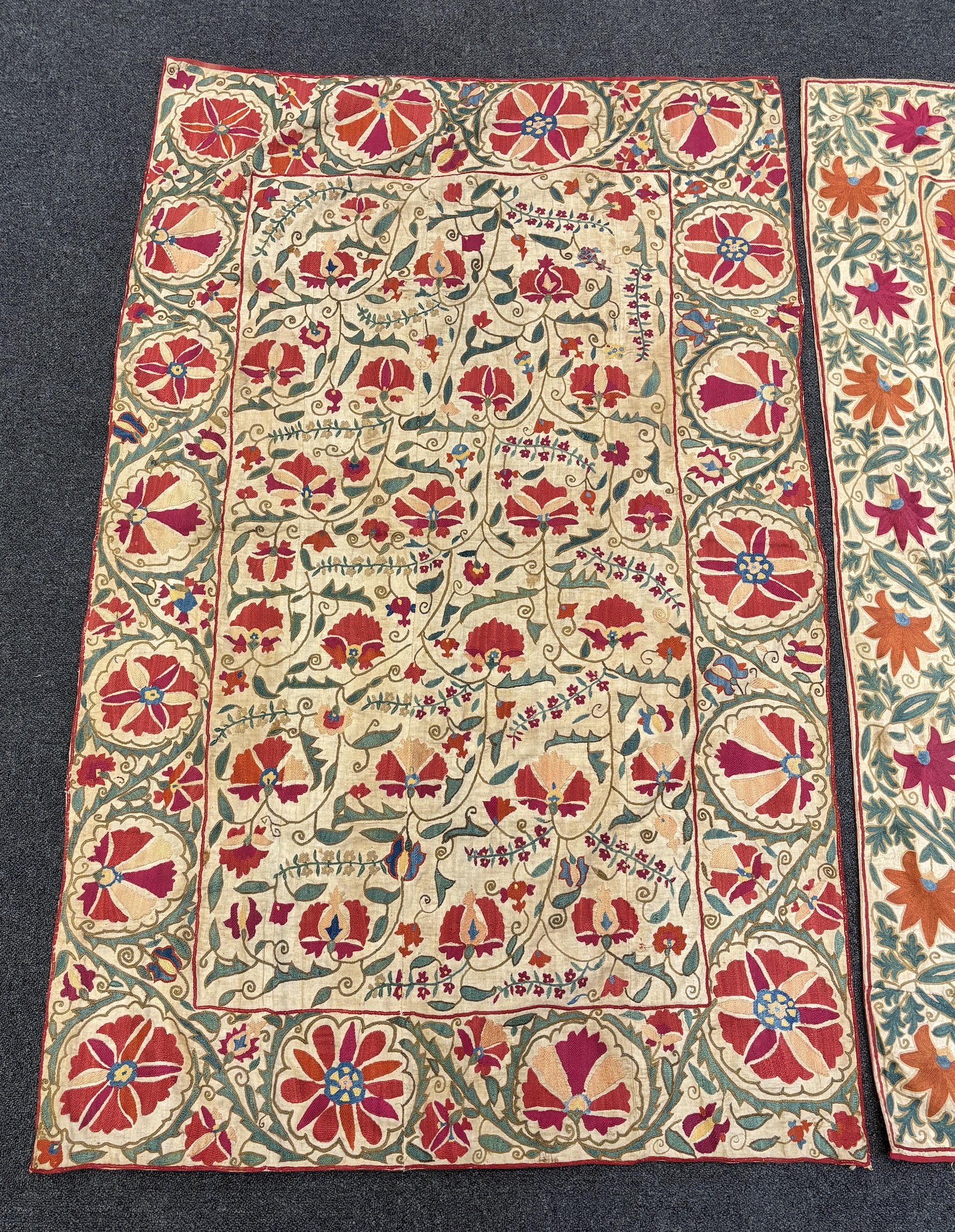 Two Uzbekistan Suzani, late 19th / early 20th century, embroidered hangings, on thick cotton, converted later to curtains, both richly embroidered with a wide floral frieze and a central all over floral design using Bukh